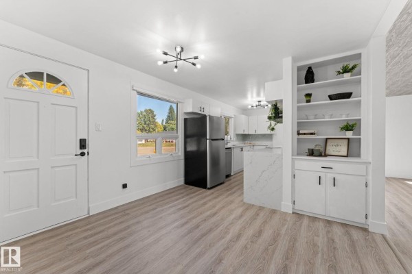 Interior view of a white hallway and entryway with a modern chandelier and a view of the kitchen. - 970 Alder Ave, Sherwood Park