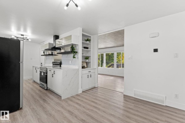 View of the kitchen with white cabinetry, stainless steel appliances, and an open doorway to a sunroom. - 970 Alder Ave, Sherwood Park