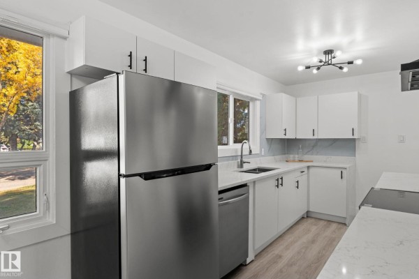 Kitchen interior featuring white cabinets, a stainless steel refrigerator, and a quartz countertop with sink. - 970 Alder Ave, Sherwood Park