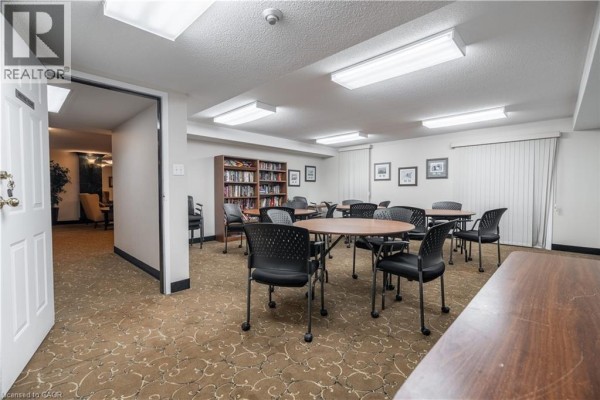 Community room with tables, chairs, bookshelves, and white blinds on windows. - 970 Golf Links Road Unit# 306, Ancaster