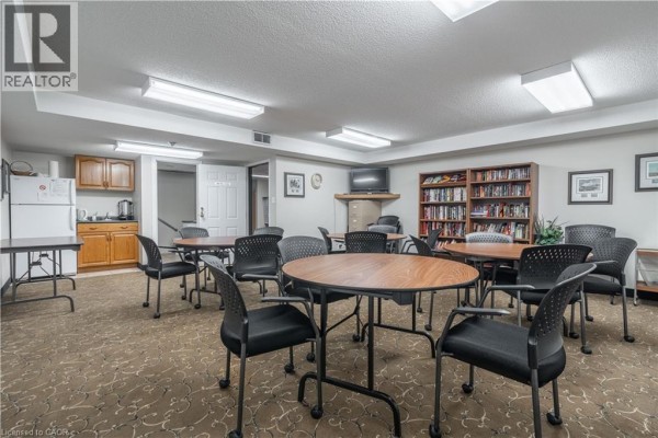 Community room with tables, chairs, bookshelves, a television, and a small kitchenette area. - 970 Golf Links Road Unit# 306, Ancaster