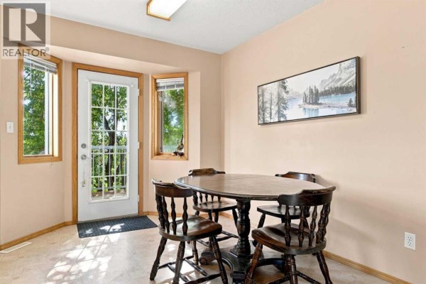 Dining area with a round wooden table and four chairs, next to a door and windows. - 9701 98 Avenue, Sexsmith