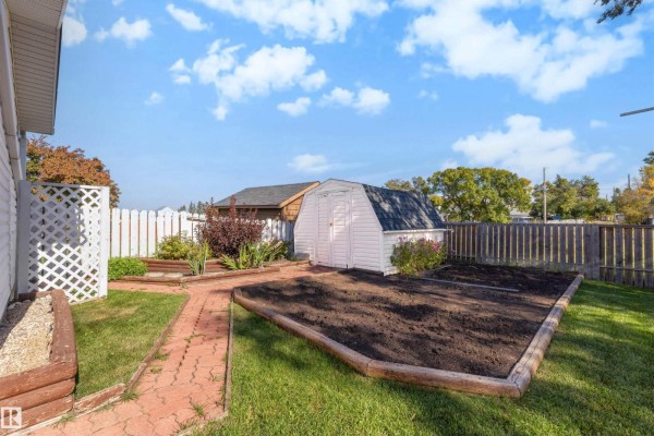 Backyard garden area with raised beds, a white shed, brick pathway, and a wooden fence. - 9703 104 St, Morinville