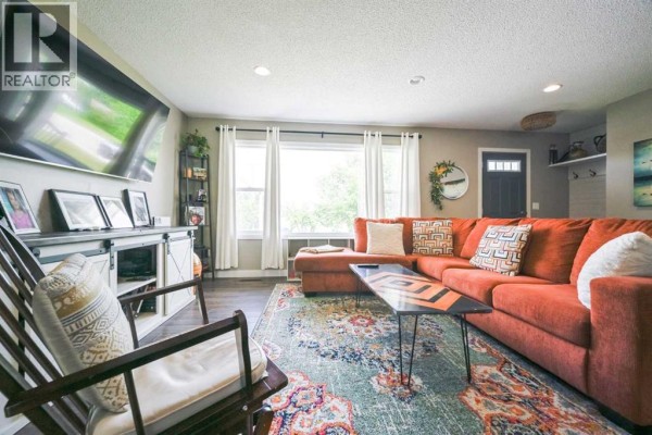 Living room with a large orange sectional sofa, coffee table, patterned rug, and rocking chair facing a TV. - 9703 87 Avenue, Grande Prairie