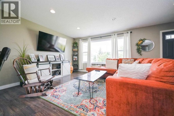 Living room with a large orange sectional sofa, coffee table, patterned rug, and rocking chair facing a TV. - 9703 87 Avenue, Grande Prairie