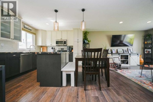 Kitchen with dark lower cabinets, white upper cabinets, a granite island with a built-in bench, and a dining table. - 9703 87 Avenue, Grande Prairie