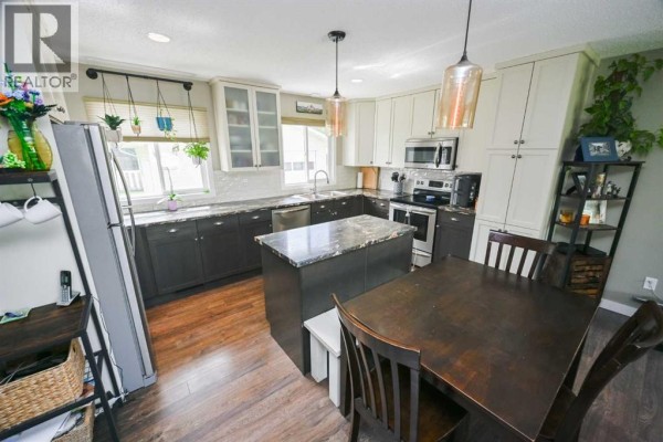 Kitchen with dark lower cabinets, white upper cabinets, a granite island, and a dining table with chairs. - 9703 87 Avenue, Grande Prairie