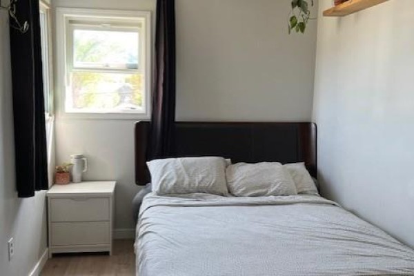 Cozy bedroom featuring a bed, bedside table, window, and minimal decor. - 9704 & 9700 Julia Street, Summerland