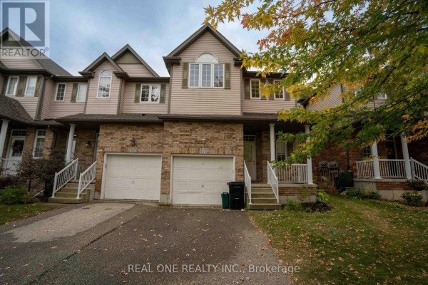 Exterior view of townhouse complex showing two garages and multiple entrances with green lawn. - 971 Creekside Drive, Waterloo