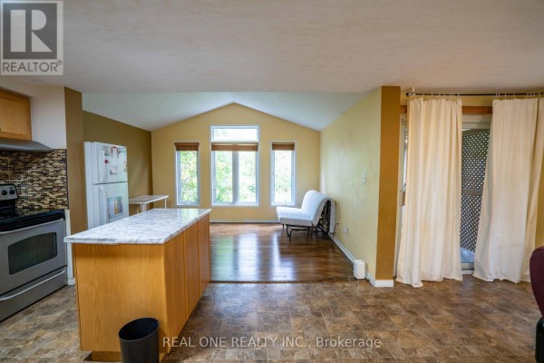 Open-concept living area with wood floors, vaulted ceiling, windows overlooking trees, and kitchen with island. - 971 Creekside Drive, Waterloo