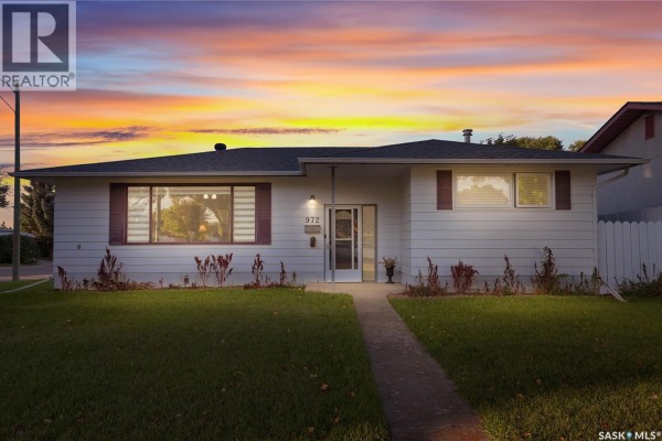 Exterior front view of the white bungalow at dusk with a colorful sunset sky. - 972 Simcoe Street, Moose Jaw