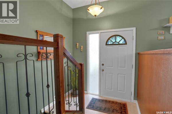 Interior view of the front entrance foyer with a white door, wood railings, and green walls. - 972 Simcoe Street, Moose Jaw