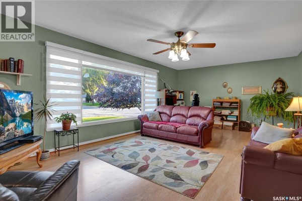 Living room with green walls, a large window, hardwood floors, a leather sofa, and a ceiling fan. - 972 Simcoe Street, Moose Jaw