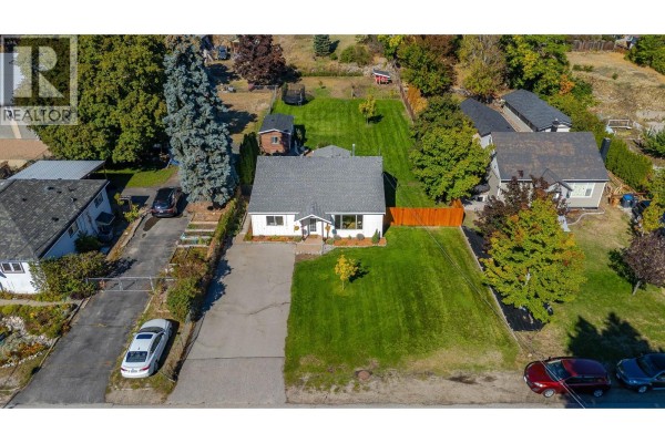 Aerial view of a white single-story house with a large green lawn, driveway, and surrounding properties. - 9722 Julia Street, Summerland