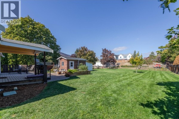 View of a large, grassy backyard with a wooden deck, shed, and distant houses. - 9722 Julia Street, Summerland