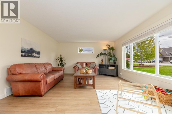 Living room with brown leather sofas, a wooden coffee table, and large windows with a street view. - 9722 Julia Street, Summerland