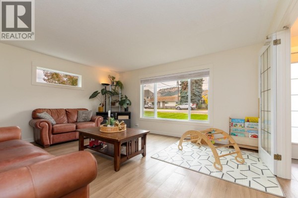 Living room with leather sofas, a wooden coffee table, a geometric rug, and a children's play area. - 9722 Julia Street, Summerland