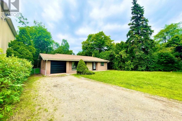 Side view of the brick house with a driveway, green lawn, and dense trees. - 9740 Keele Street, Vaughan