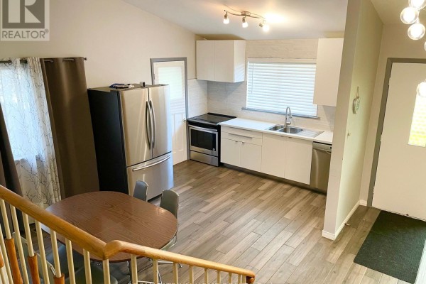Interior view of a small kitchen with white cabinets, stainless steel appliances, and a dining table. - 9740 Keele Street, Vaughan