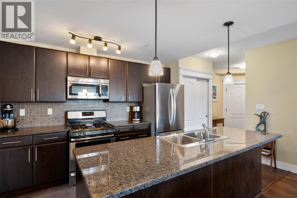 Modern kitchen with dark wood cabinets, granite countertops, stainless steel appliances, and tile backsplash. - 975 Victoria Street W Unit# 606, Kamloops