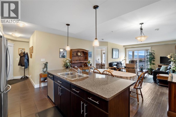 View of the kitchen island, dining table, and living area with hardwood floors and neutral paint. - 975 Victoria Street W Unit# 606, Kamloops