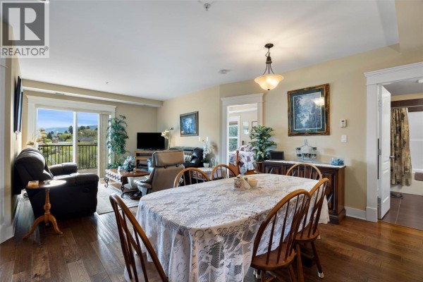 Dining area with a lace-covered table and chairs, leading to the living room and balcony. - 975 Victoria Street W Unit# 606, Kamloops