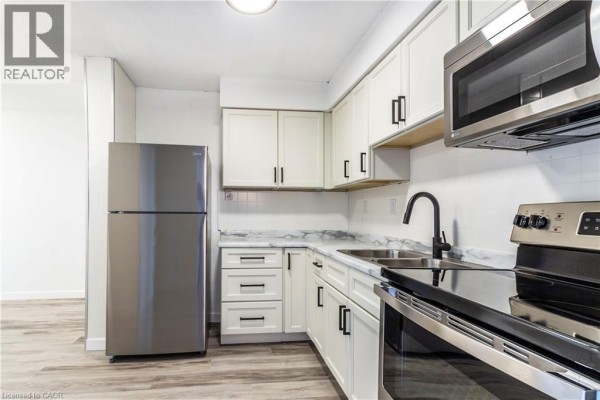Kitchen with stainless steel fridge, black stove, and marble countertops, emphasizing modern design. - 975 Warwick Court Unit# 908, Burlington