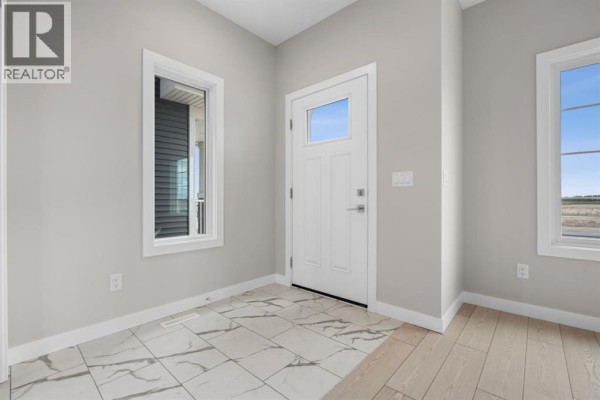 Foyer with light gray walls, white trim, marble-look tile flooring, and a white front door. - 9755 Huxbury Drive Ne, Calgary