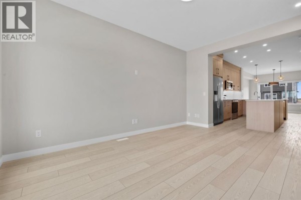 View from dining area into open-concept kitchen with light wood cabinets and stainless steel appliances. - 9755 Huxbury Drive Ne, Calgary