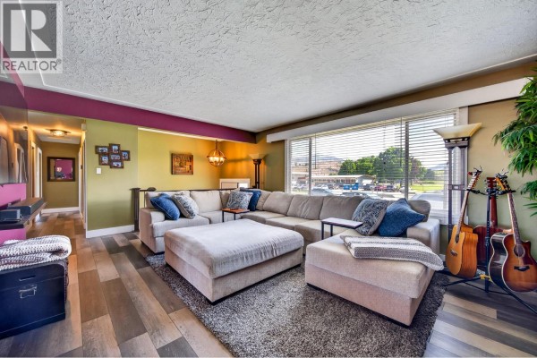 Living room with a large sectional sofa, fireplace, and guitars leaning against the wall. - 976 Holt Street, Kamloops