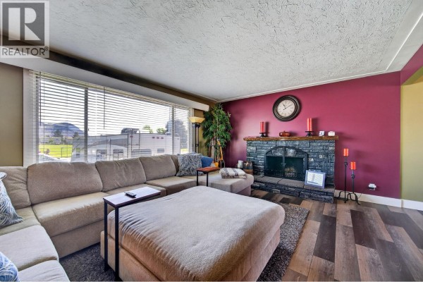 Living room featuring a stone fireplace, large windows, and a sectional sofa with ottomans. - 976 Holt Street, Kamloops