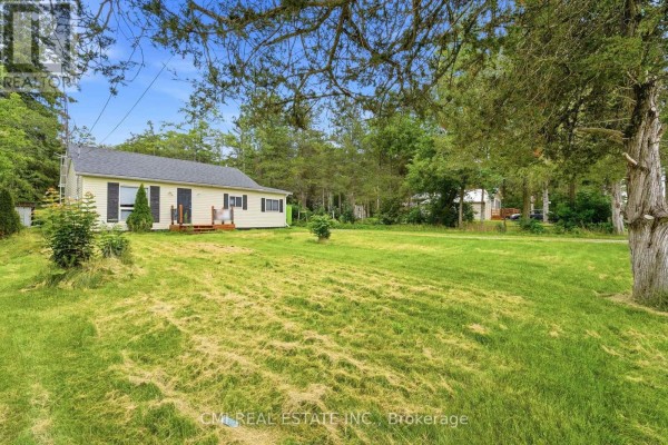 Side view of the yellow bungalow with a large green lawn and trees. - 977 County Rd 38, Trent Hills