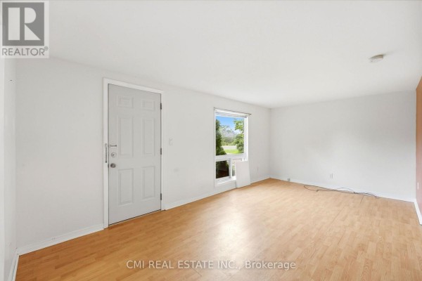 Interior of a room with white walls, a window overlooking greenery, and a wood-look floor. - 977 County Rd 38, Trent Hills