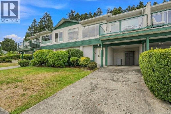 Exterior of a two-story townhouse complex with a covered carport and manicured hedges. - 977 Highview Terr, Nanaimo