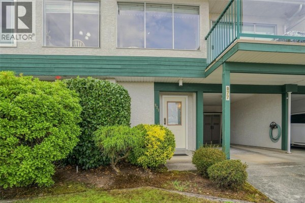 Close-up of the townhouse entrance with a light beige door and green trim, surrounded by shrubs. - 977 Highview Terr, Nanaimo