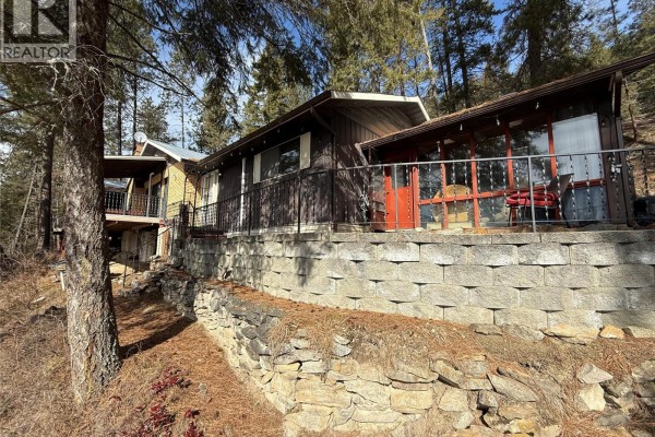 Stone retaining wall supporting a house with wooden siding and a sunroom. - 9779 3a Highway, Kuskanook