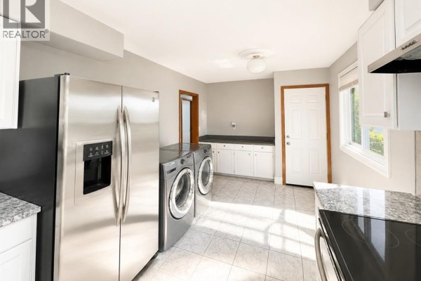 Laundry room with stainless steel refrigerator, washer, dryer, white cabinets, and a doorway. - 979 Arthur Road Unit# Main, Windsor