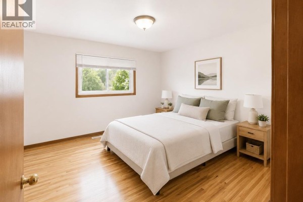 Bedroom with a queen-size bed, wooden floors, nightstands, and a window overlooking trees. - 979 Arthur Road Unit# Main, Windsor