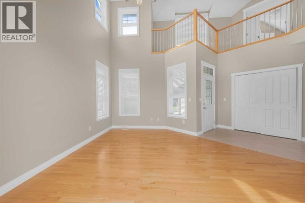 Empty living room with hardwood floors, beige walls, large windows, and a view of the upper landing. - 98 Canals Circle Sw, Airdrie