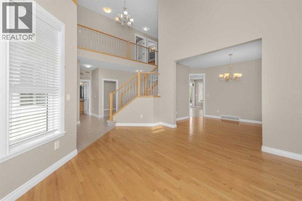 Spacious living and dining area with hardwood floors, beige walls, and views of the staircase and hallway. - 98 Canals Circle Sw, Airdrie