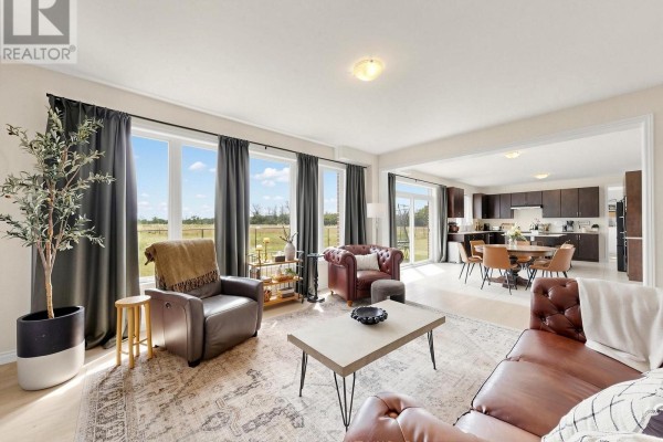 Living room with leather sofas, coffee table, and large windows overlooking a field. - 98 Golden Meadows Drive, Otonabee South Monaghan