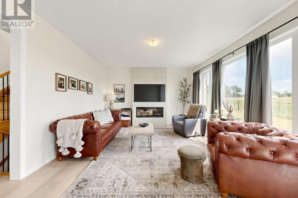 Living room with leather furniture, fireplace with TV, and large windows with field views. - 98 Golden Meadows Drive, Otonabee South Monaghan