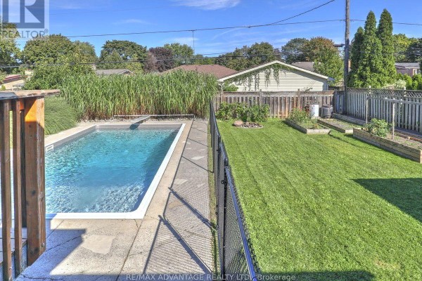 View of a backyard with a swimming pool, fence, green grass, and garden beds. - 98 Goldwick Crescent, London East