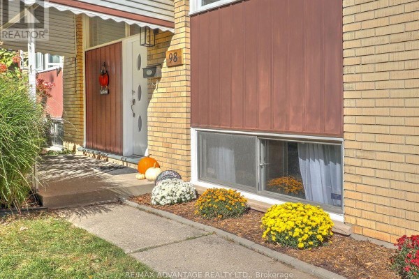 Front door with address number 98, brick facade, and decorative fall flowers. - 98 Goldwick Crescent, London East