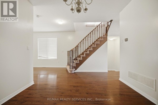 Living area with hardwood floors, a wooden staircase, and white walls. - 98 Teal Crest Circle, Brampton