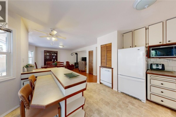 View of the kitchen, dining area with wooden table, and living room with wood stove. - 980 Coats Dr, Gabriola Island