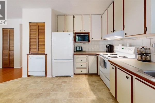 Kitchen area with white appliances, light brown cabinetry, and tile flooring, showing stove and refrigerator. - 980 Coats Dr, Gabriola Island
