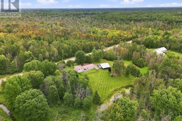 Aerial view of the property showing the house, garage, outbuildings, pond, and surrounding forest. - 980 County Rd 44, North Grenville