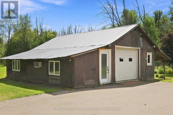 Exterior of a detached garage with a white overhead door, glass door, and metal roof. - 980 County Rd 44, North Grenville