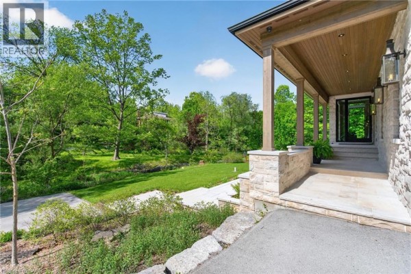 Covered front porch with stone pillars, stone facade, and glass double doors leading inside. - 981 Mineral Springs Road, Ancaster